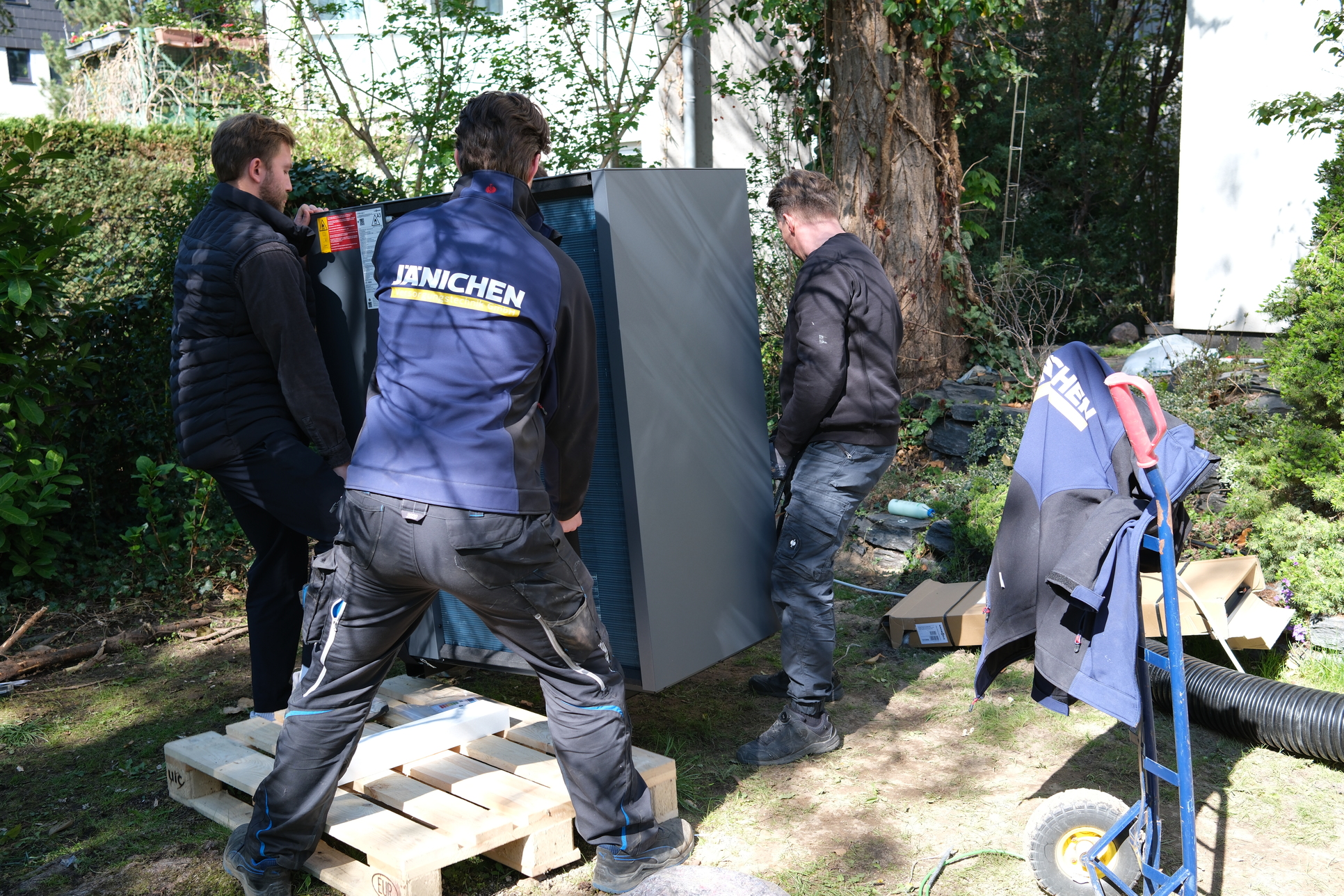 Jänichen Monteure tragen eine neue Wärmepumpe zum Aufstellort im Garten, Berlin
